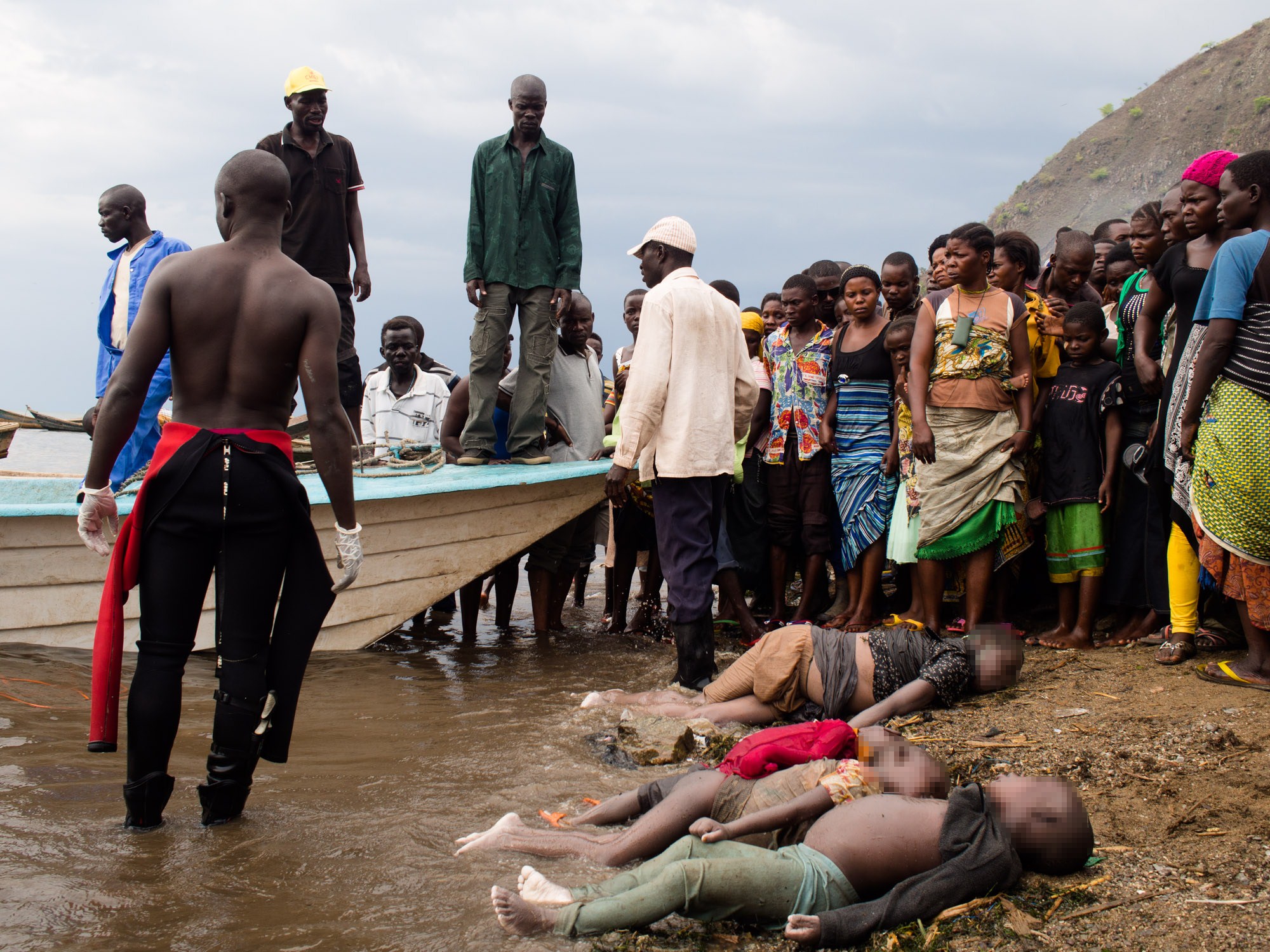 GRAPHIC CONTENT People stand near the bodies retrieved by the Ugandan Police divers, on the shore of Lake Albert in Kitebere landing site on March 23, 2013. As many as 60 people are feared to have drowned when a boat capsized on Lake Albert on the border between Uganda and Democratic Republic of Congo, reports said on March 22. Uganda's Daily Monitor newspaper said the boat, travelling between two districts in western Uganda, capsized shortly before midday Saturday. "We have also recovered 19 bodies but we expect more bodies," local official Oscar Chunyai was quoted as saying. He added that dozens more people had been rescued by fisherman who saw the accident. The boat was reportedly carrying 100 people, many of them refugees from the DRC, The New Vision newspaper said, adding that 15 bodies of children had also been recovered. The number rescued so far pointed to a potential death toll of anywhere between up to 50 or 60 dead, Ugandan media reports said. AFP PHOTO/Michele Sibiloni (Photo credit should read MICHELE SIBILONI/AFP/Getty Images)